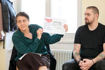 Fotografie - Kinderbeirätin Fabienne und Alexander, ehemaliger Bewohner von NOAH, Barbora Pokorny, Leiterin der Obdachlosenunterkunft NOAH und Alexander, ehemaliger Bewohner. Frau Pokorny hält den Ausdruck aus einer PowerPoint-Präsentation hoch, auf dem die Abkürzung NOAH erläutert wird: niedrigschwellig, ortsnah, Anspruch auf Heimat