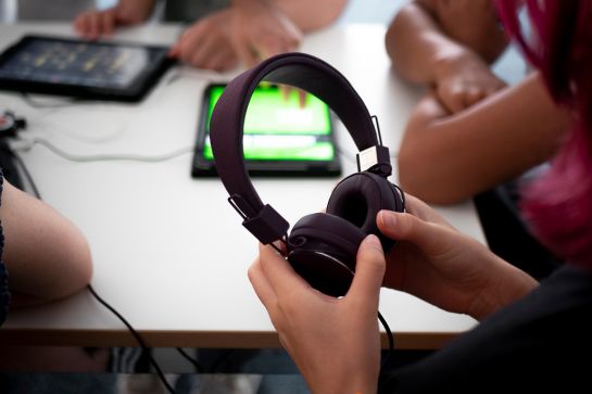 Person sitzt mit anderen am Tisch und hat Kopfhörer in den Händen (C) Andrea Borowski