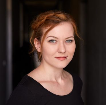 Portrait einer Frau mit roten Haaren, blauen Augen und heller Haut, die in die Kamera schaut.