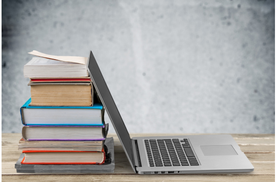 Fotografie - ein Laptop steht an einen Stapel Bücher gelehnt