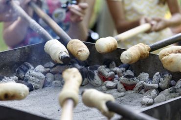 Fotografie - Kinder backen Stockbrot an langen Stecken über großem Holzkohlegrill