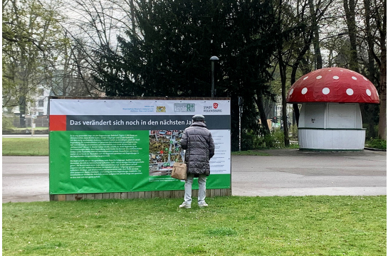 Frau steht vor Informationsschild. Im Hintergrund der Milchschwammerl.