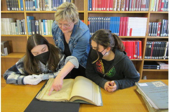 Fotografie: Die Archivpädagogin zeigt zwei Schülerinnen etwas in einem alten Buch.
