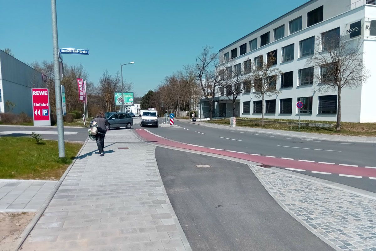 Fotografie - Baumaßnahme Hermann-Köhl-Straße/Wernerwerkstraße - Die kombinierte Ein- und Ausfahrt zum bestehende Lebensmittelmarkt wurde auf das notwendige Maß verbreitert. Die auf dem Bild zu sehende eingebaute Mittelinsel soll zudem das Queren der Straße erleichtern; für den Radverkehr wurde ein Schutzstreifen angelegt                           