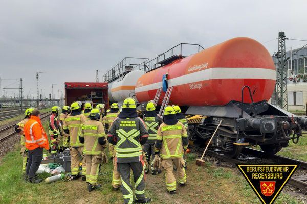 Einsatzkräfte in Schutzkleidung stehen vor dem Kesselwagen