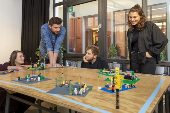 Fotografie: Zwei Männer und zwei Frauen versammeln sich um einen Tisch mit Lego-Bauwerken. (C) Bilddokumentation Stadt Regensburg