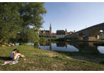 Fotografie - zwei Personen sitzen auf einer Wiese an der Donau, im Hintergrund die Steinerne Brücke