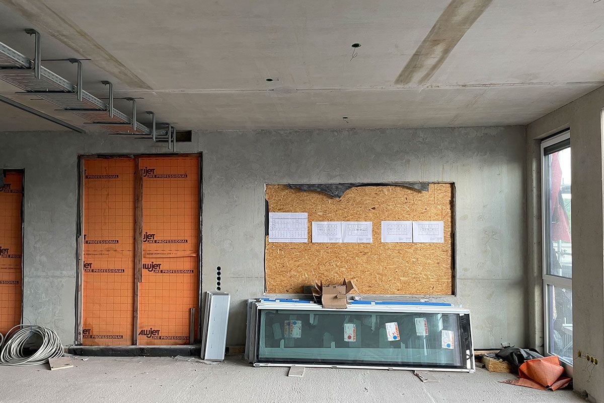 Fotografie - Aufnahme aus dem künftigen Speisesaal (Aufenthaltsraum) im 1. OG. Hinter der Holzverkleidung wird bereits jetzt gekocht, hier entsteht später eine große Durchreiche von der Küche im bereits fertigen Bauabschnitt 3a. Hinter der orangen Folie schließt sich der Flur an.