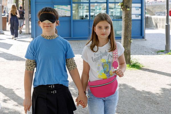 Fotografie - Ein Mädchen aus dem Kinderbeirat mit Blindenbinde wird von einem weiteren Mädchen aus dem Kinderbeirat an der Hand geführt