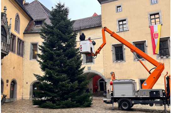 Fotografie: Zwei Männer heben mit einem Hubsteiger den Weihnachtsstern auf den Christbaum am Rathausplatz.