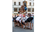 Fotografie: Ein junger Mann mit freiem Oberkörper macht einen Salto über sechs gebückte Menschen.