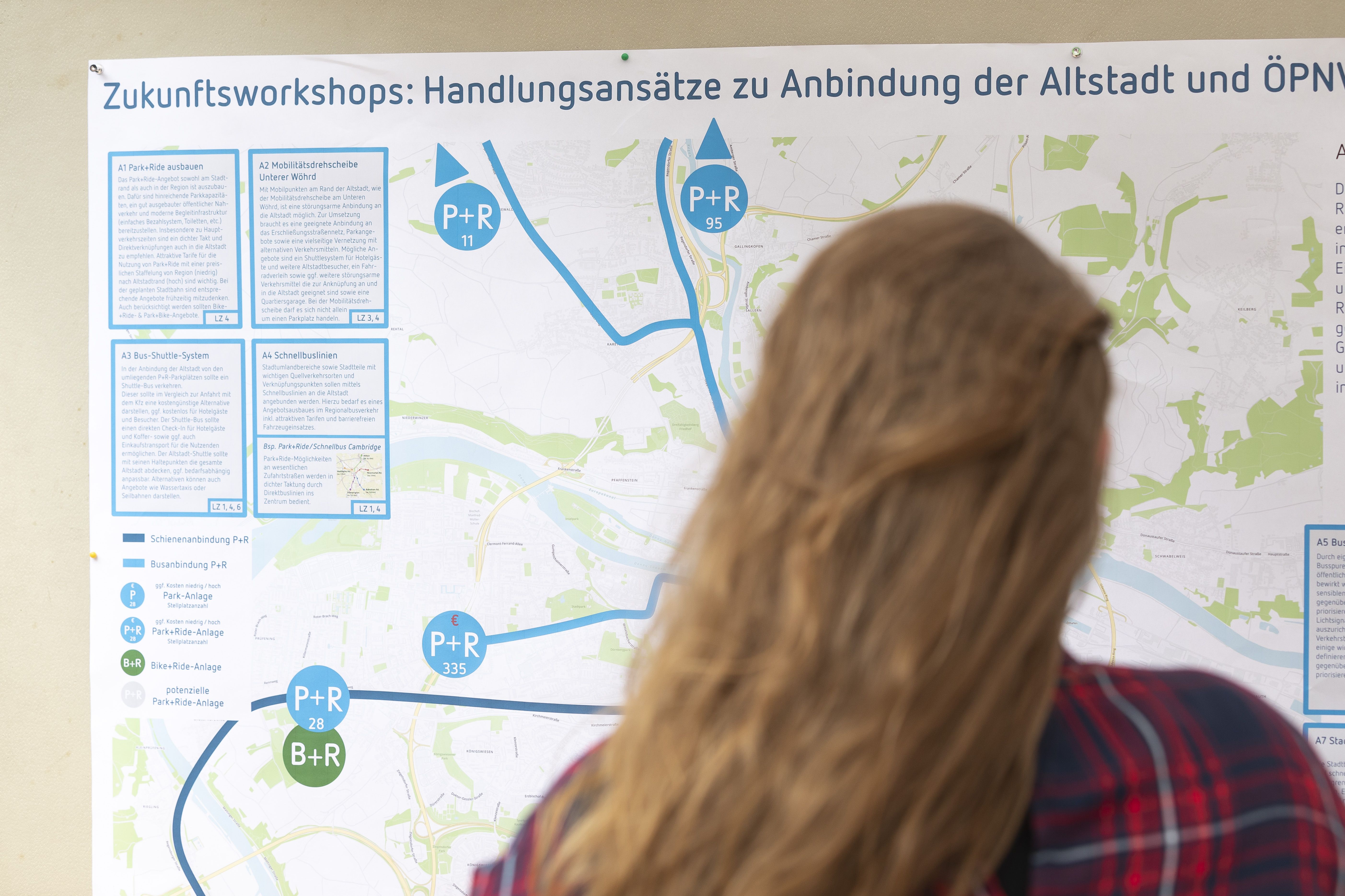 Fotografie: Das Foto zeigt eine Frau, die gerade eine Stellwand mit Informationen zum Projekt „Verkehrsberuhigung Altstadt“ betrachtet. 