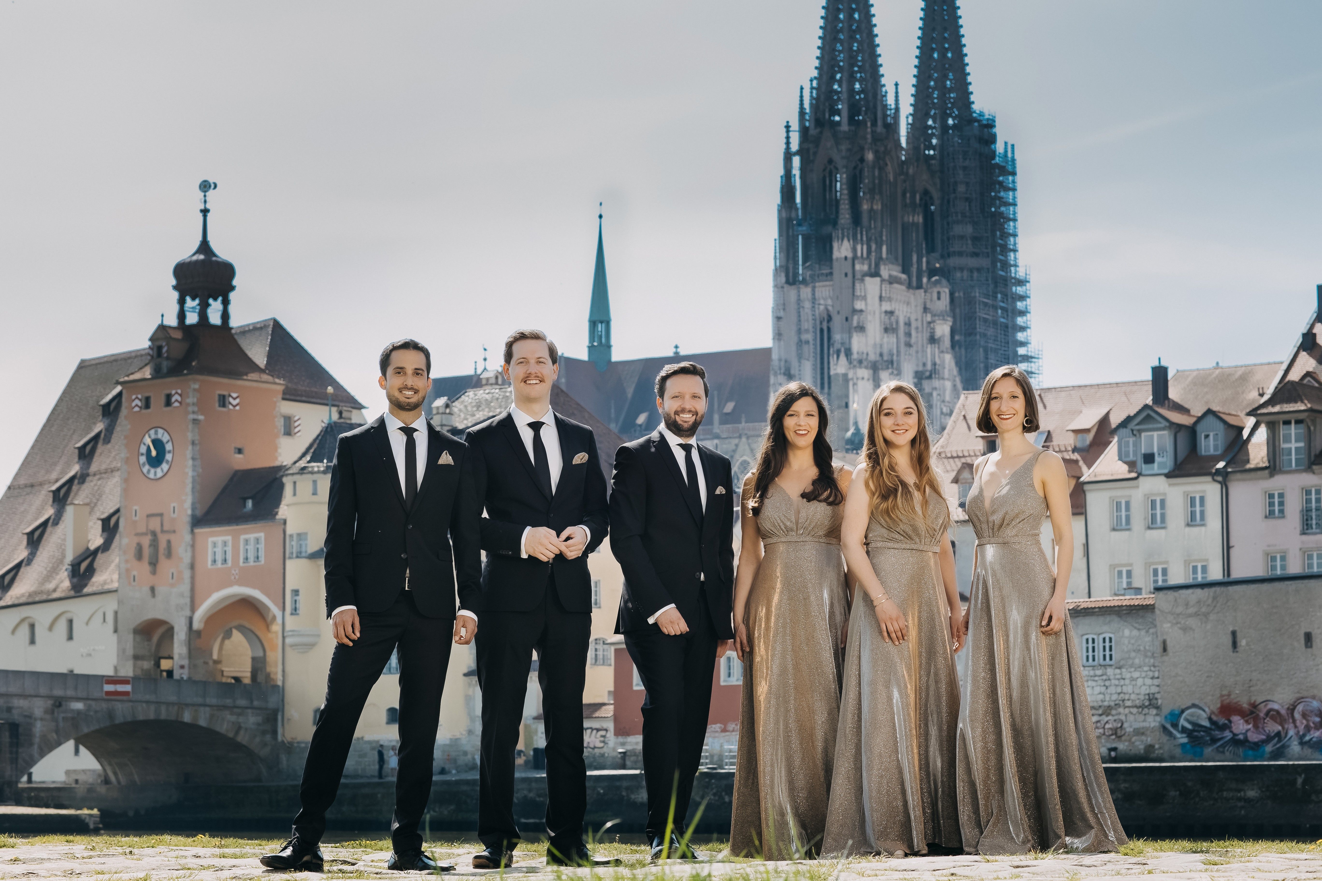 Fotografie – das Vokalensemble StimmGold steht vor der Kulisse der Steinernen Brücke und des Doms. Das Ensemble besteht aus drei Männern und drei Frauen