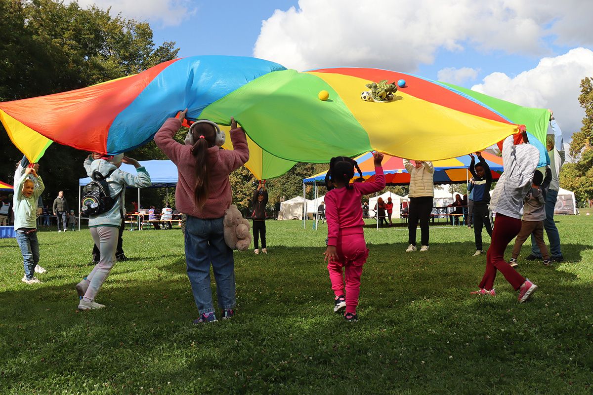 Zu sehen sind mehrere Kinder die gemeinsam mit einem bunten Schwungtuch spielen.                                                  