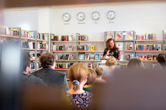 Foto einer Frau am Stehpult, die Zuhörern in der Bücherei etwas vorträgt. (C) Andrea Borowski