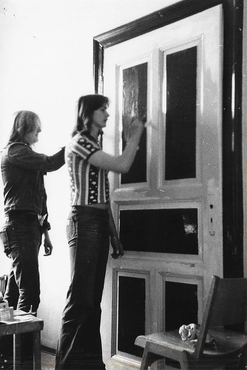 Zu sehen sind zwei Männer, die im Rahmen einer Arbeitsmaßnahme der Kontaktstelle für Arbeit eine Tür lackieren.                            