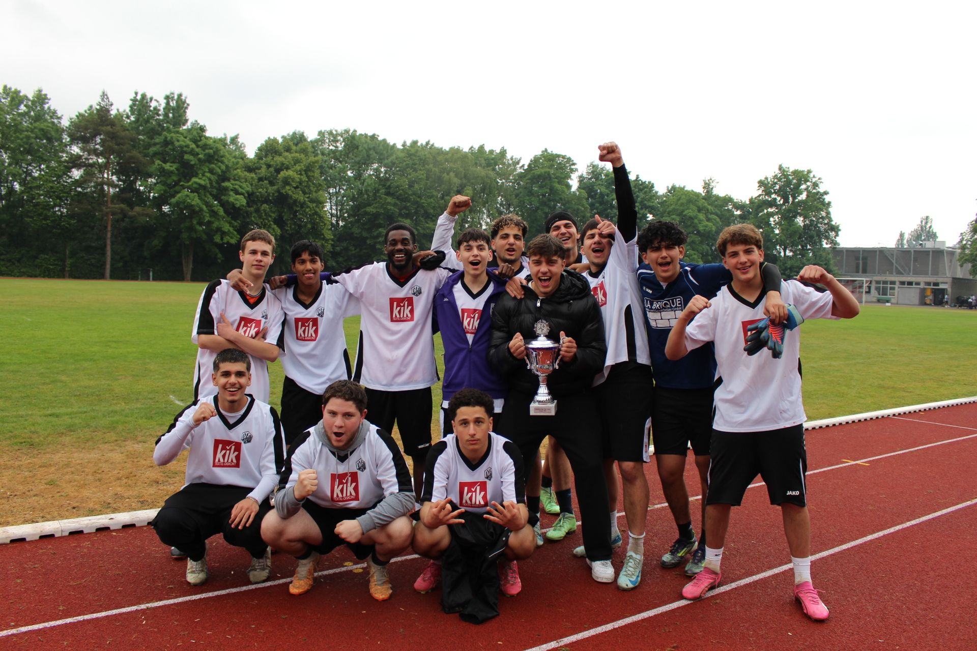 Jugendliche mit Siegespokal auf einem Fußballplatz
