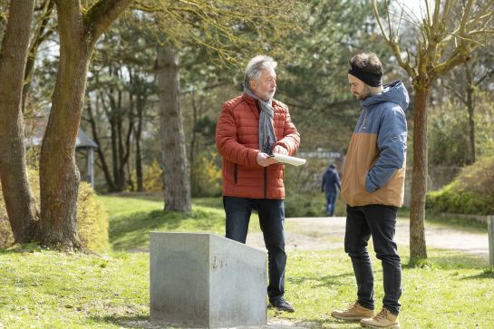 Fotografie: Stadtheimatpfleger Prof. Gerhard Waldherr erläutert einem Mann am Kumpfmühler Geschichtsquader die spannende Geschichte des ehemaligen römischen Kohortenlagers.