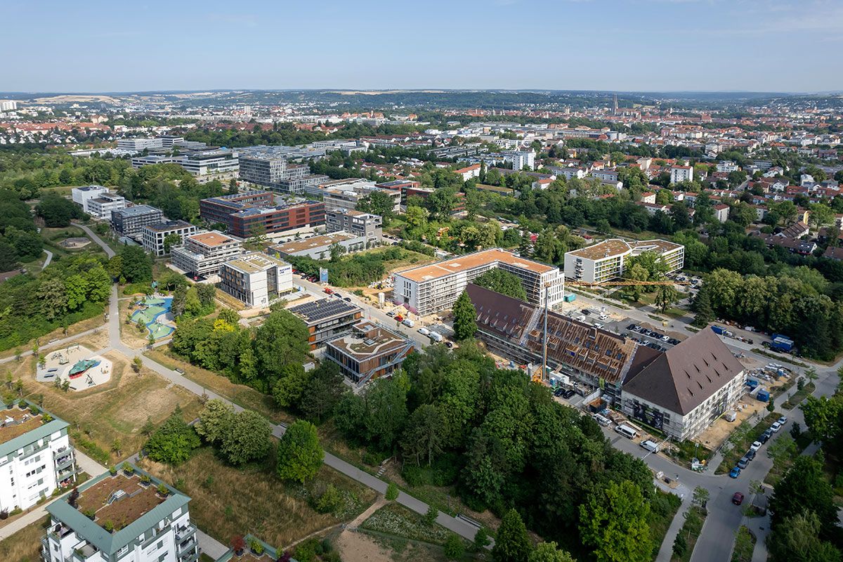 Fotografie - Blick von Südost nach Nordwest auf das gesamte TechCampus-Areal. Im Vordergrund ist die Mischgebietsbesiedlung mit dem Motto „Arbeiten und Wohnen“ zu sehen; am rechten Bildrand die Entwicklung des denkmalgeschützten Gebäudekomplexes „Nibelungen-Terassen“. Oben links – eher im Hintergrund ist die TechBase zu sehen, oben rechts die Silhouette der Altstadt.