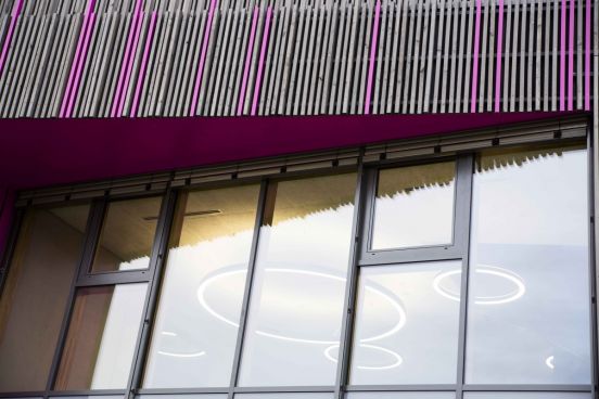 Fotografie - Blick von Außenseite des Hauses durch große Fensterfront, innen sind mehrere runde Ringlampen an der Decke befestigt
