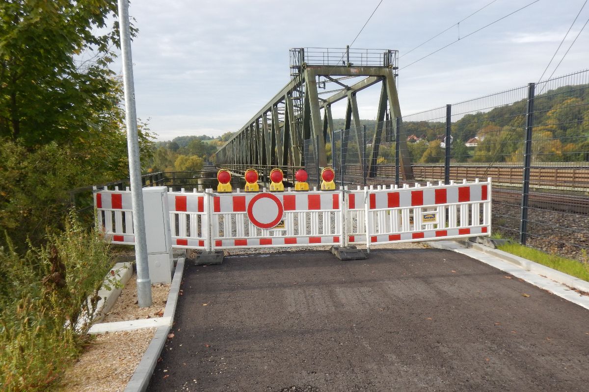 Auf dem Bild sieht man rechterhand den bereits angebrachten Schutzzaun. Der abgesperrte Bereich grenzt an die Widerlager bzw. Brückenpfeiler der Sinzinger Geh- und Radwegbrücke an. Entsprechende Asphaltierungsarbeiten des Weges folgen.