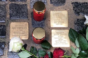 Fotografie - eingebaute Stolpersteine mit Kerzen und Rosen geschmückt
