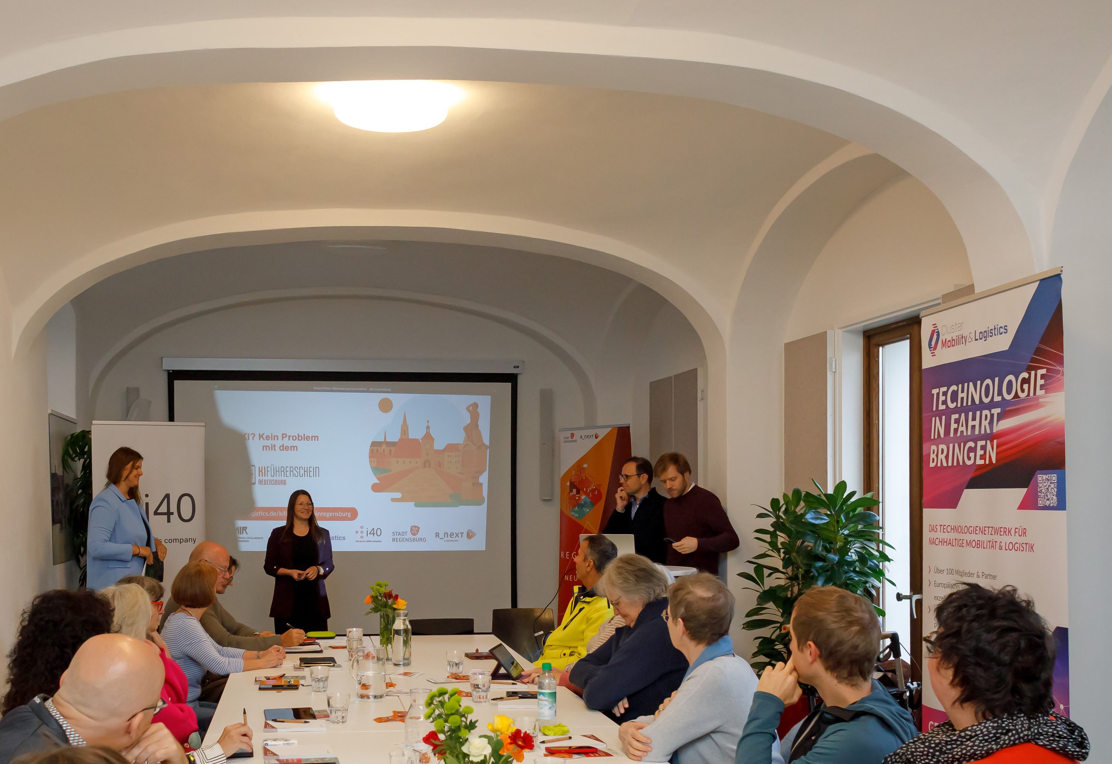 Das Bild zeigt den Workshopraum im Schreiberhaus: Dort sitzen die Teilnehmenden an einem langen Tisch und schauen in die Richtung der Präsentation.