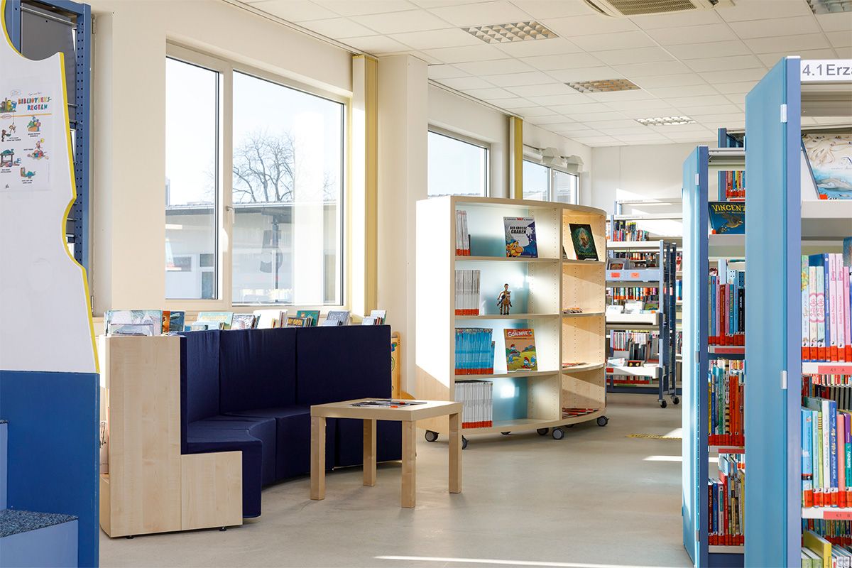 Zu sehen sind eine halbkreisförmige Sitzbank für Kinder mit Comics in den Regalen