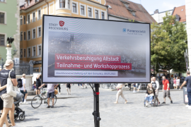 Fotografie: Das Foto zeigt einen auf dem Domplatz aufgebauten Bildschirm mit einer Präsentation mit dem Titel „Verkehrsberuhigung Altstadt - Teilnahme- und Workshopprozess“.