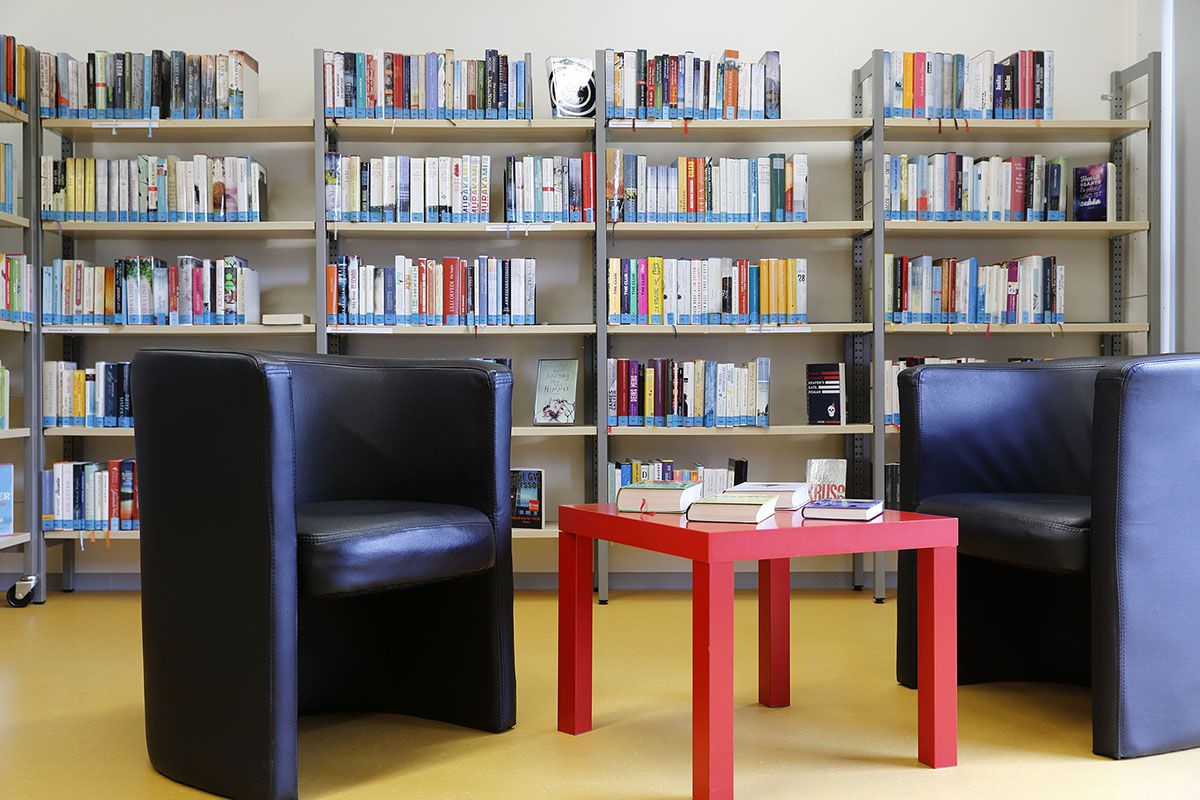 Foto zwei Sessel und ein Tisch. Im Hintergrund Bücherregale