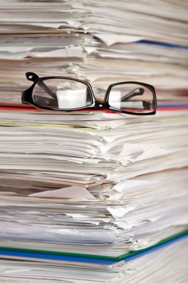 Symbolbild - Papierstapel mit Brille
