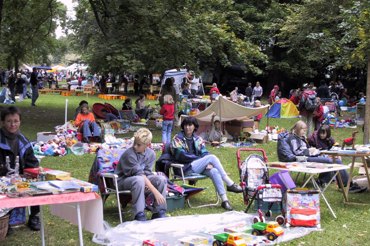 Zu sehen sind verschiedene Flohmarktstände im Park, an denen Familien Spielzeug, Schultaschen, Kinderwägen und andere, für Familien nützliche, Dinge verkauft werden.                                                     