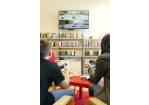 zwei Jugendliche spielen Videogames, im Hintergrund Bücherregale mit Jugendbüchern