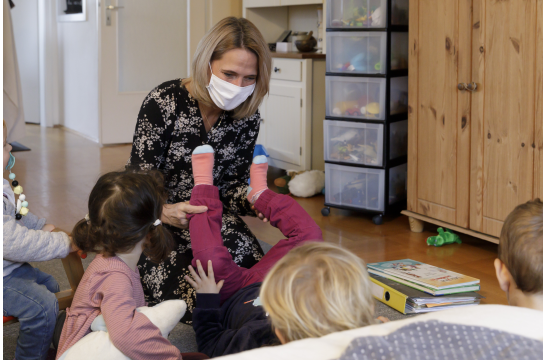 Fotografie – Tagesmutter spielt mit Kindern in Wohnzimmer