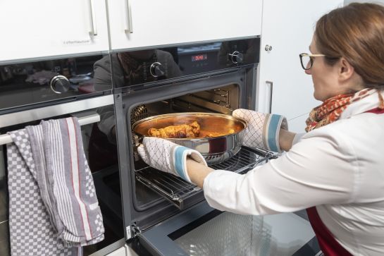 Fotografie: Eine Frau schiebt einen Braten in den Backofen.