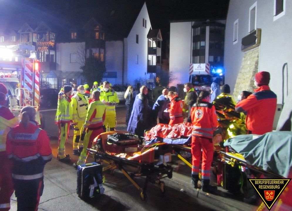 Fotografie: Einsatzkräfte von Rettungsdienstorganisationen mit ihrer Ausrüstung vor einem Mehrfamilienhaus.