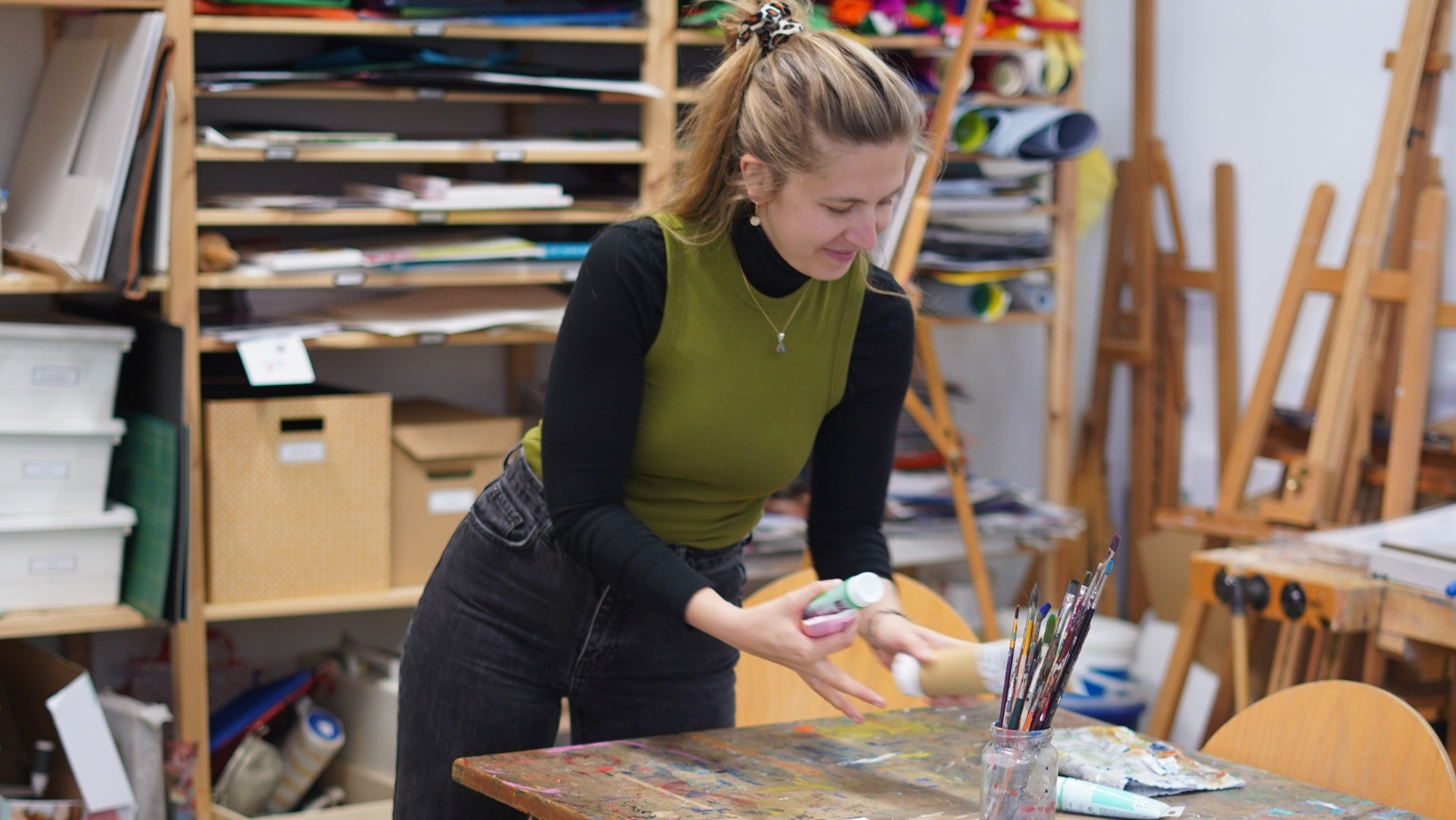 Auf dem Bild ist Sara Peßler vor einem großen Holzregal im Atelier des W1 zu sehen. Sie ist gerade dabei, ein Bild zu malen.