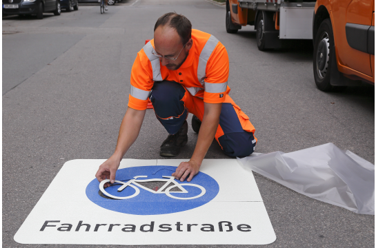Ein Mitarbeiter der Stadt Regensburg bringt einen Bodenaufkleber "Fahrradstraße" auf der Fahrbahn auf. 