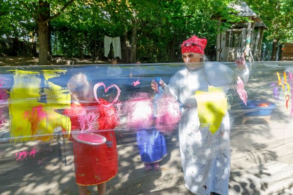 Fotografie: Eine Erzieherin und ein Kind besprühen eine Plastikfolie im Garten.
