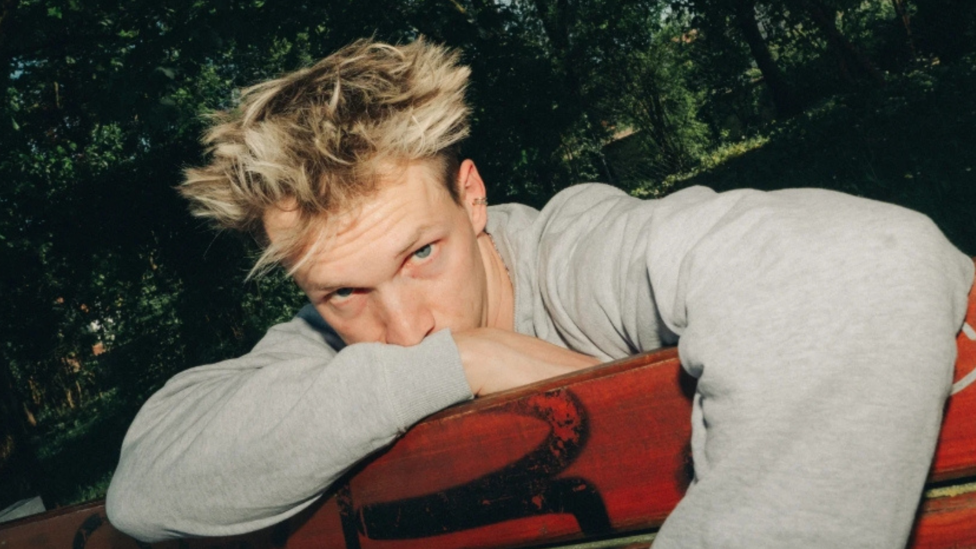 auf dem Foto sieht man den Künstler Lenzelot. der auf einer roten Couch sitzt und sein Gesicht halb darüber hinausragt, nachdenklich. 