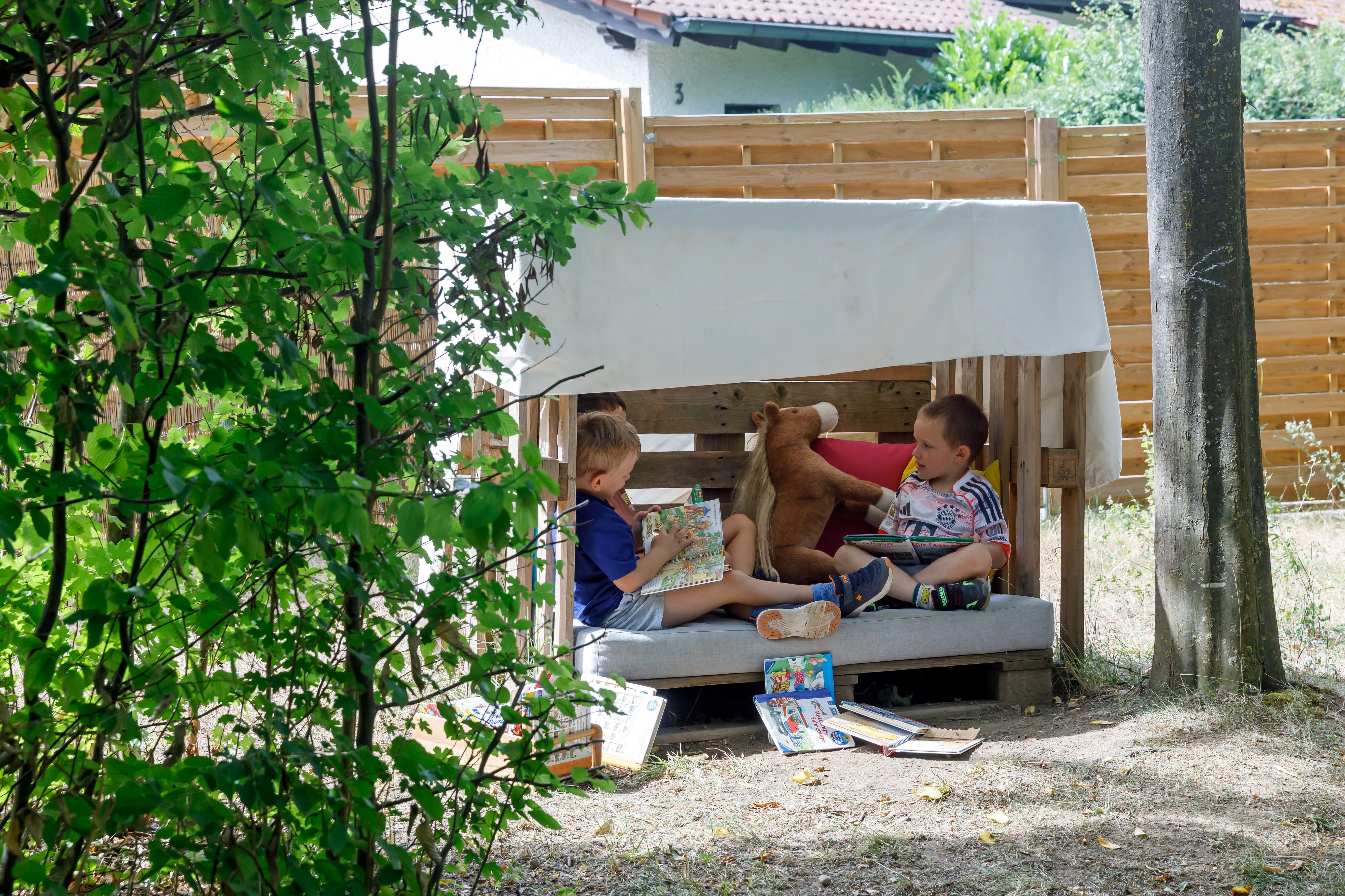 Fotografie: Kinder sitzen in einer Leseecke im Garten.