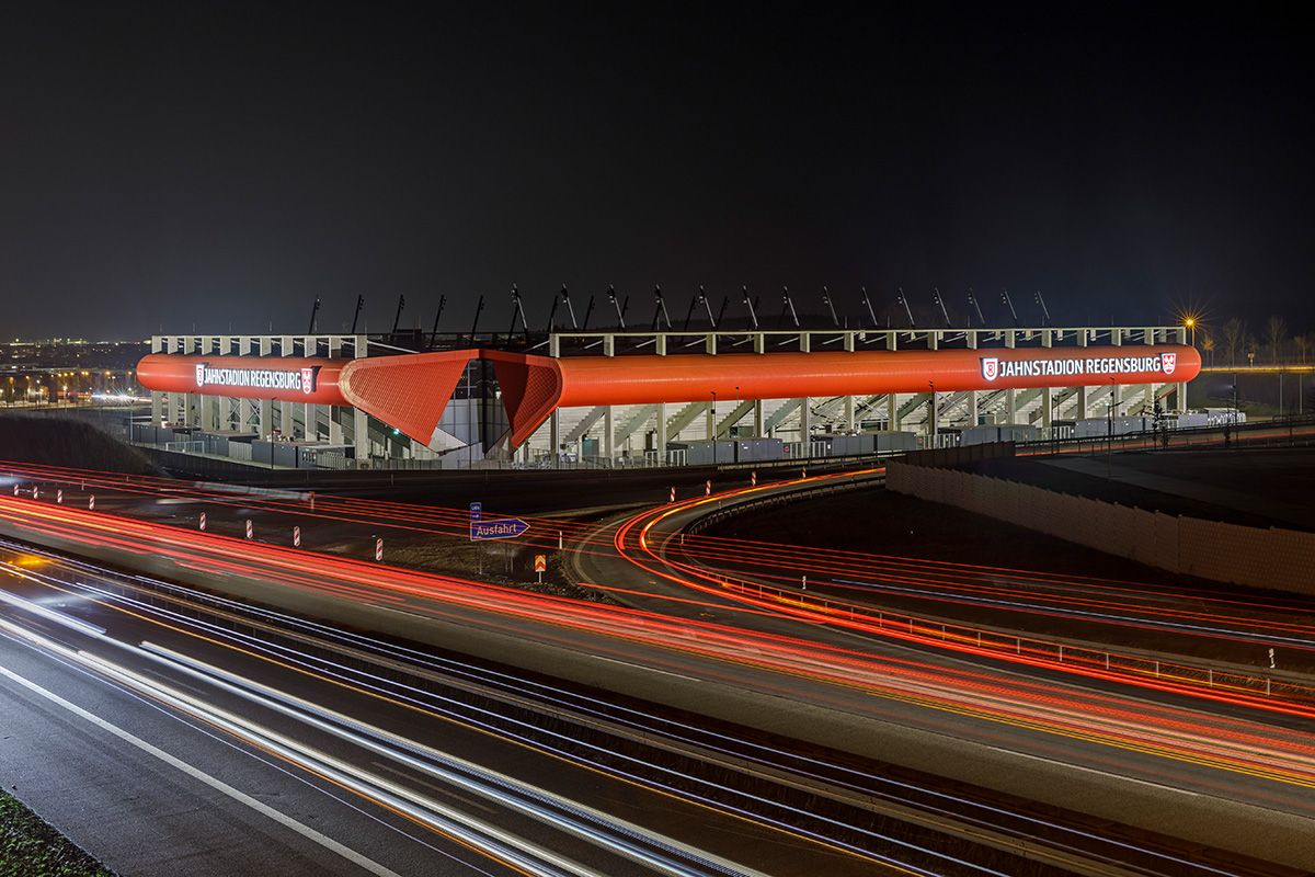 Fotografie - das Regensburger Jahnstadion leuchtet in der Nacht, im Vordergrund die Autobahn
