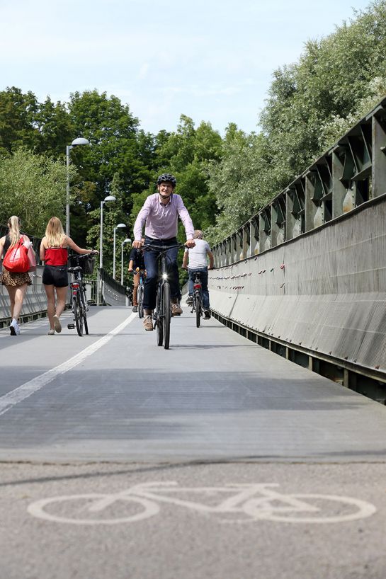 Fotografie: Thomas Großmüller fährt mit seinem Fahrrad auf dem Grieser Steg direkt auf die Kamera zu. Er trägt einen Helm. Im Hintergrund sind Passanten zu sehen. 