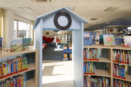 halbkreisförmiges Bücherregal mit hellblauem Tor, darauf ist ein Bullauge montiert und führt in die neugestaltete Kinderbücherei Burgweinting