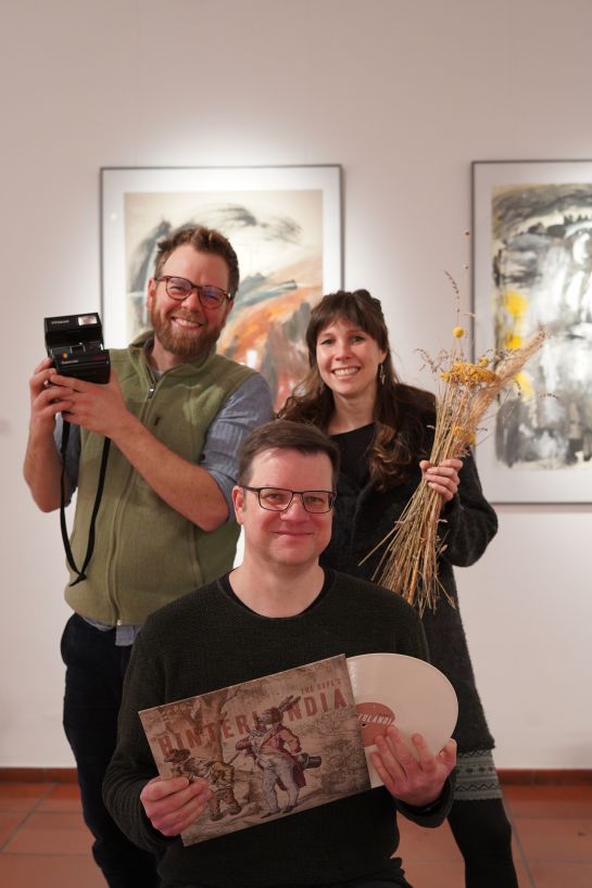 Das Team des W1, aufgenommen in der Galerie mit spartentypischen Gegenständen in den Händen (Dominik Huber mit Fotokamera, Bianca Kurz mit einem Strauch Kräuter und Blumen, Matthias Segerer mit einer Schallplatte).