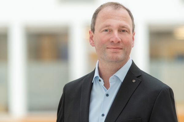 Man erkennt einen Mann im Anzug, der in die Kamera lächelt.