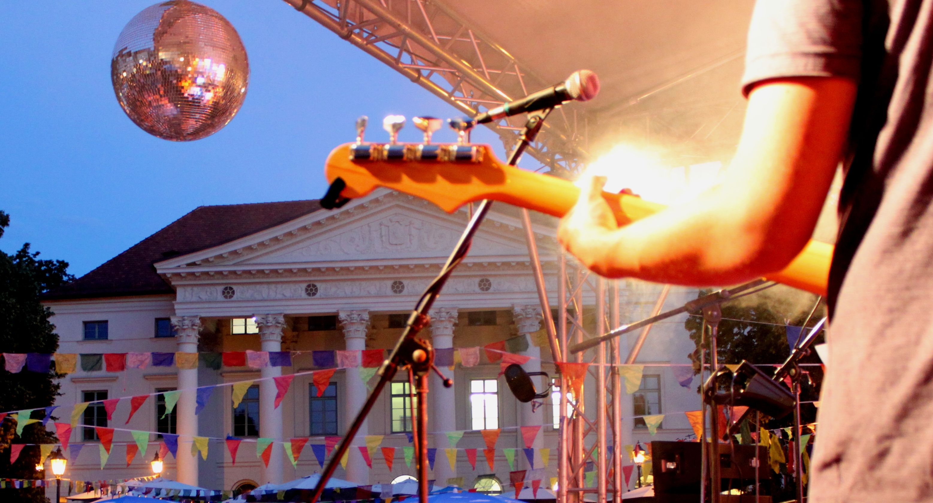 W1-Bühne auf dem Bismarckplatz mit Bassisten von hinten unter einer Spiegelkugel vor dem mit Wimpeln geschmückten Platz.
