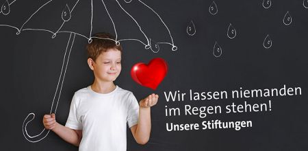 Themenbild Städtische Stiftungen - Symbolbild - kleiner Junge steht vor einer Tafel, auf der ein Regenschirm und Regentropfen gemalt sind und ein rotes Herz schwebt über seiner linken Hand