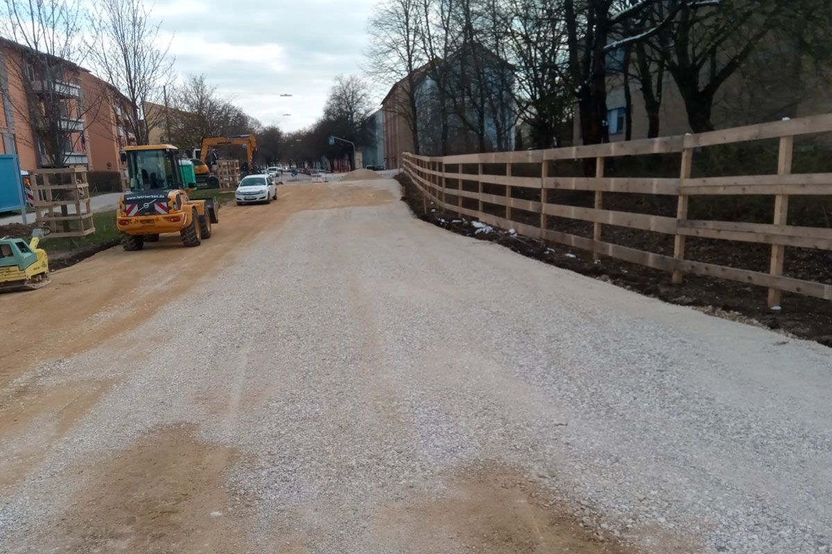 Fotografie - unterster Teil der Baustraße, im Hintergrund Anschluss an die Aussiger Straße; die Frostschutzplanie ist fertig auf Höhe ausgerichtet und Baustraße somit bereit für die kommende Aspahltierung; am rechten Bildrand Baumschutz-/Grundschutzzäune