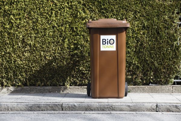 Fotografie: Eine braune Biotonne steht vor einer Hecke auf dem Gehweg.